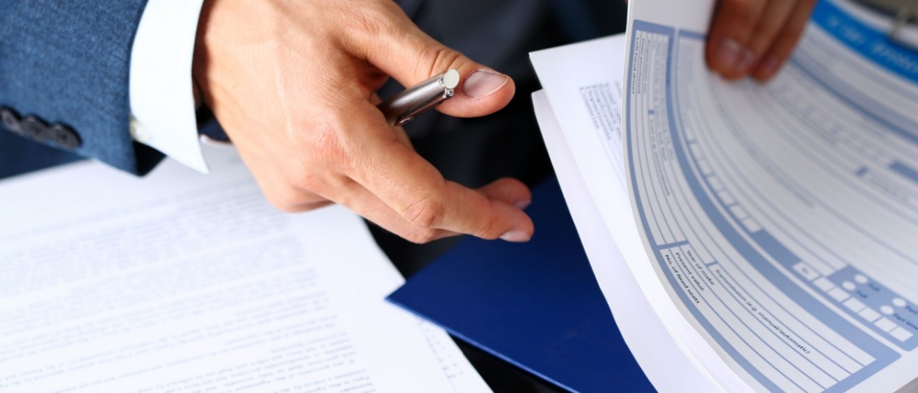 Male arm in suit offer insurance form clipped to pad and silver pen to sign a renters insurance.