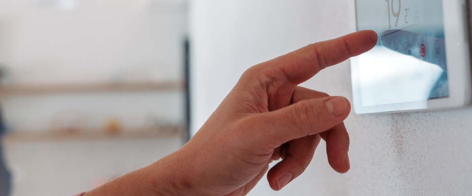 Close up of a person’s hand adjusting a touchscreen thermostat in a smart home.