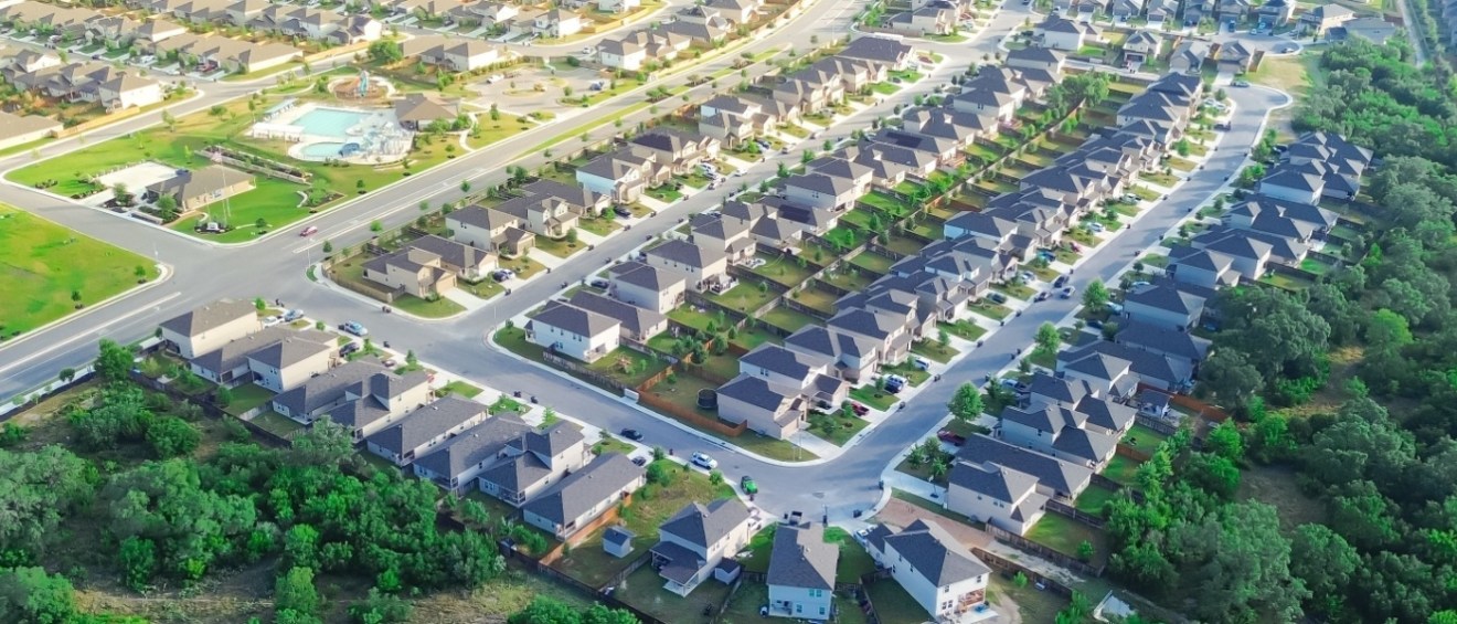 Aerial view of a housing community, with green spaces, wide street and community swimming pool.
