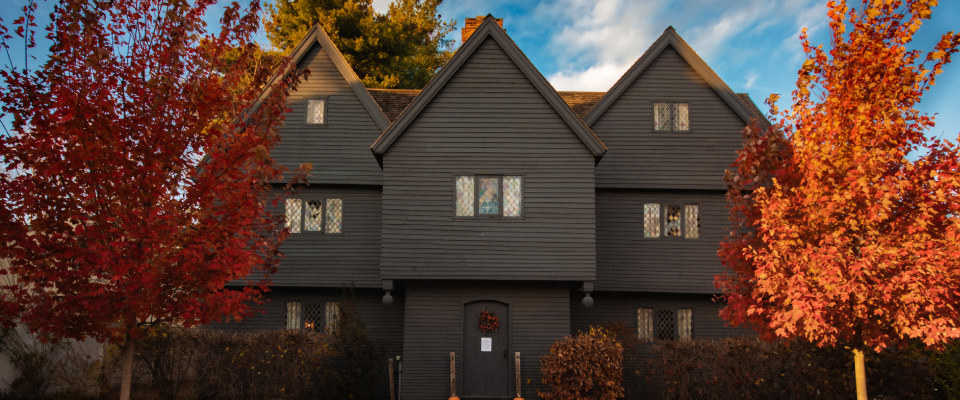 The Witch House of Salem during the fall, with two trees with orange and red leaves in the front yard.