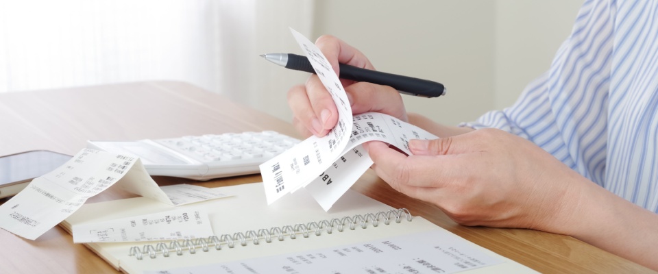 Close-up of a person holding some receipts and calculating their expenses.