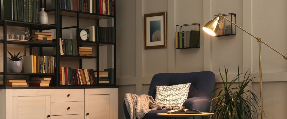 A cozy indoor library, with an armchair in the foreground and a large bookshelf along the wall.