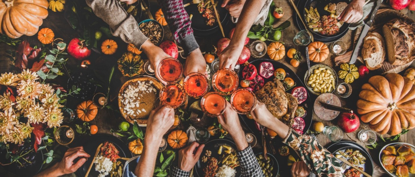 A bountiful Thanksgiving dinner spread, with plenty of food options including turkey or pumpkin, and a group of friends toasting their drinks.