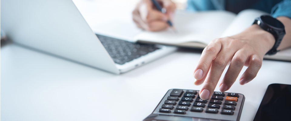 A close-up of a businesswoman working at an office desk, using a calculator to manage home finances.