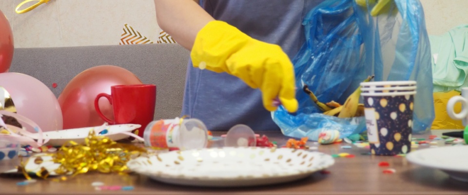A woman tidying up a messy living room after a birthday party, surrounded by remnants of the celebration.