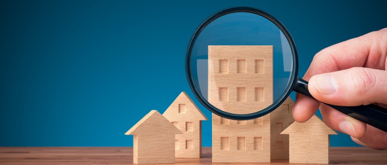 Magnifying glass inspecting a wooden apartment model, symbolizing scrutiny in debunking myths about renting.