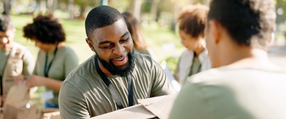 A volunteer in a park organizing cardboard boxes filled with donations for distribution as part of a community service or charity event. 
