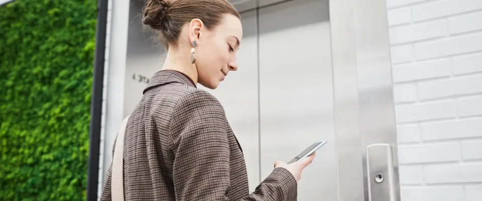 A minimalistic, low-angle shot of a young businesswoman standing in a modern office building, waiting for an elevator. 