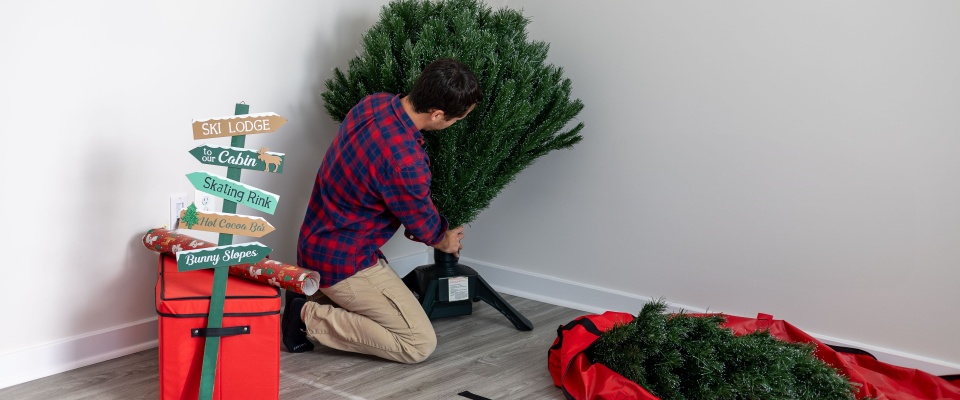 A young man setting up a Christmas tree in his house, carefully arranging branches and ornaments.