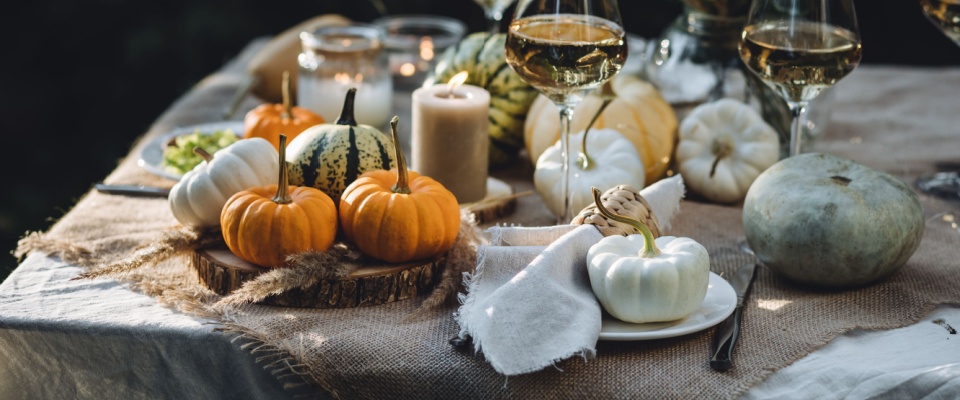 A cozy outdoor table setup for a Thanksgiving family dinner or romantic autumn wedding, decorated with small pumpkins, warm glowing candles, and seasonal fall accents.