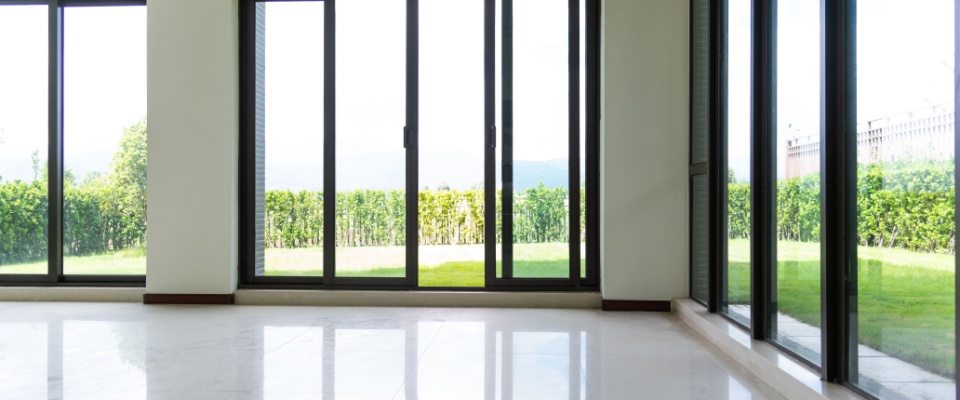 An empty living room in a house, featuring large windows that let in natural light. 