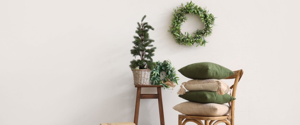 A cozy home interior featuring a comfortable chair with decorative pillows, a mini Christmas tree on a nearby table, and a mistletoe wreath hanging on the wall. 