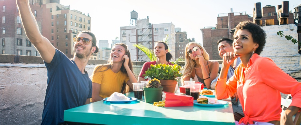 A group of young, happy friends enjoying a barbecue dinner on a rooftop in New York City.