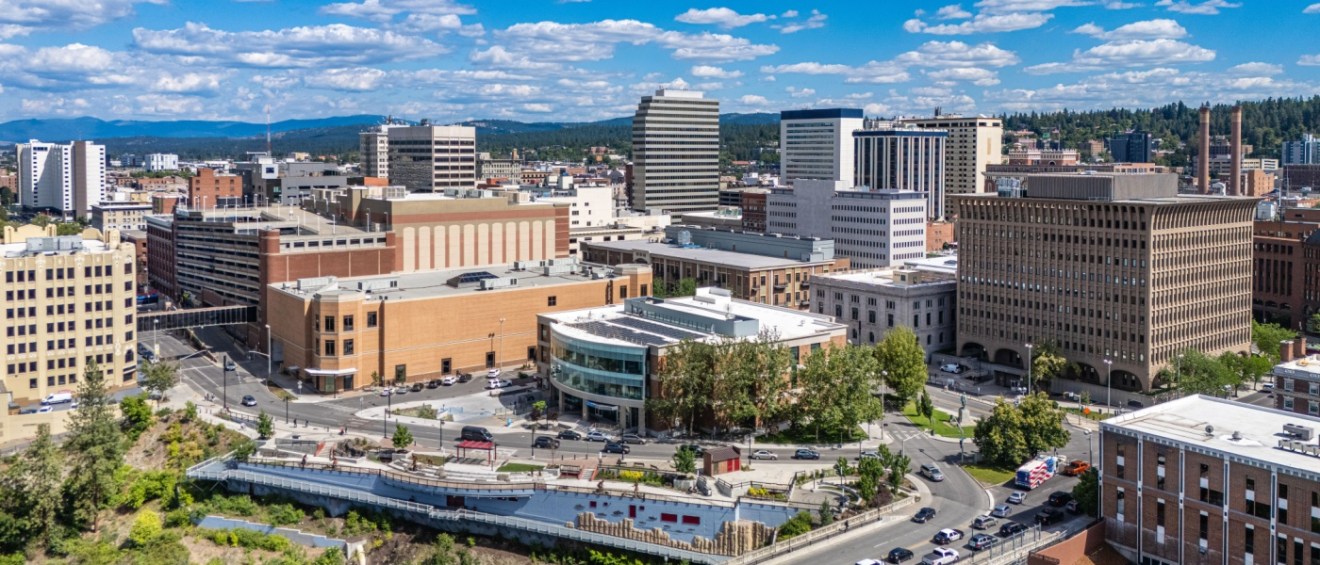 An aerial view of downtown Spokane, Washington, showcasing a mix of modern and historic buildings surrounded by lush greenery.
