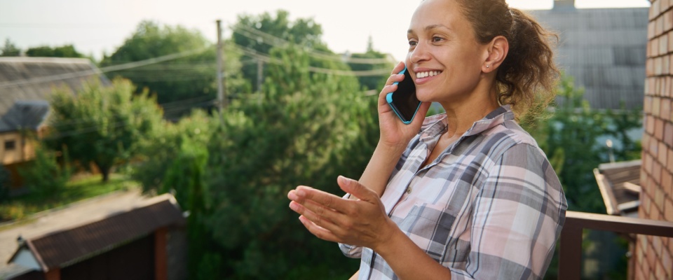 A woman standing on the balcony of her home, talking on a mobile phone. 