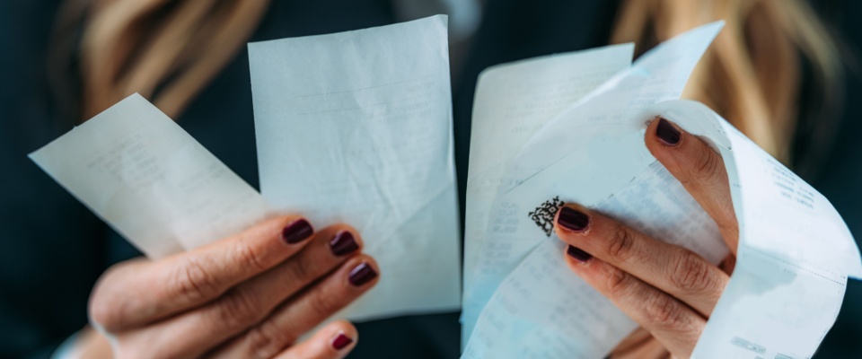 A close-up of a person’s hands, holding a few shopping receipts as they examine their expenses.