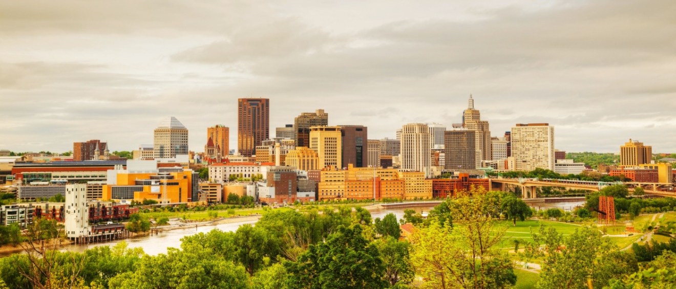 Downtown St. Paul, MN skyline with greenery and the Mississippi River in the foreground. Find the best affordable neighborhoods in St. Paul, MN.