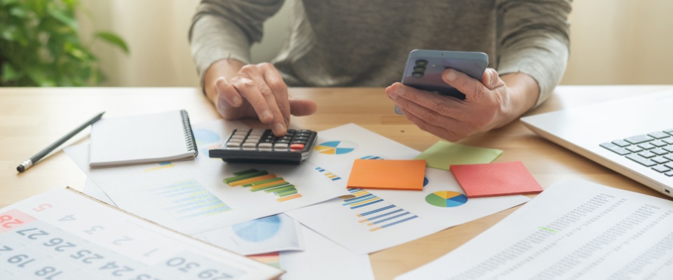 A woman at home multitasking with her phone and calendar, using a scheduling app to organize appointments, plan events, pay bills, and set goals.