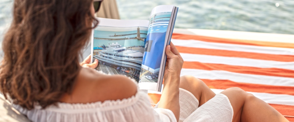 A woman sitting comfortably in a cabana on the beach, reading a marine magazine.