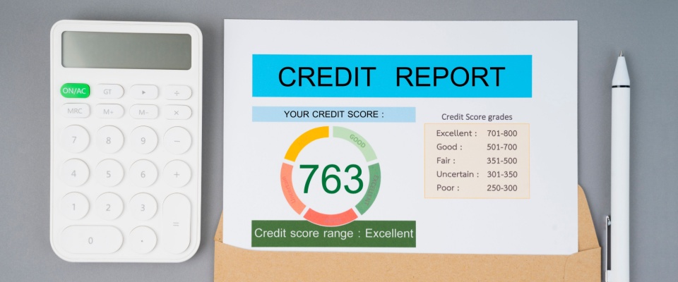 An image of a calculator on the left-hand side, a pen on the right-hand side, and between them is an open envelope with a credit report sticking out of it.