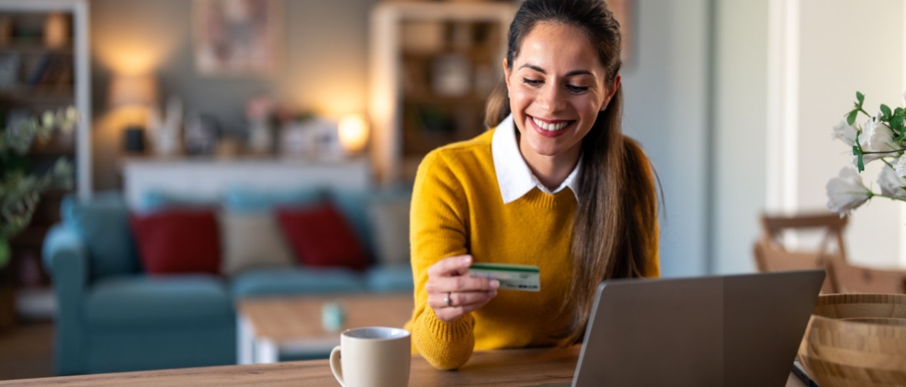 A charming businesswoman sitting at a desk in her home office, using a laptop. She holds a credit card in her hand, reflecting a seamless and convenient shopping experience in a professional yet comfortable setting.