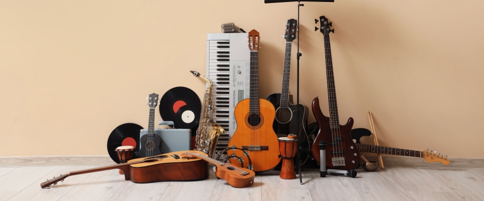 A collection of various musical instruments arranged near a beige wall. The instruments include a guitar, violin, keyboard, and others, showcasing a diverse range of musical styles and creating a harmonious and creative atmosphere.