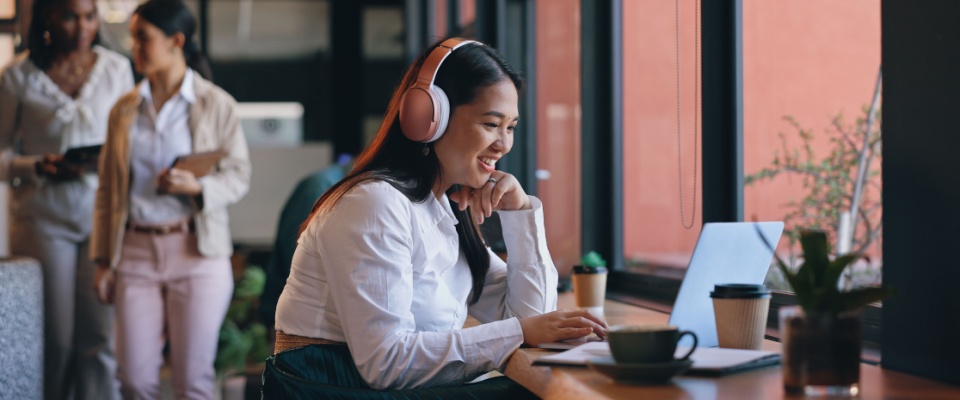 A young Asian woman working on her laptop in a coffee shop, managing her freelance career as an editor or publisher.