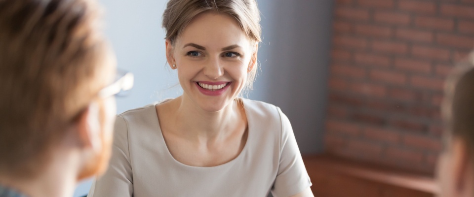 A confident millennial businesswoman smiling warmly during a business meeting, engaging with a male partner. 