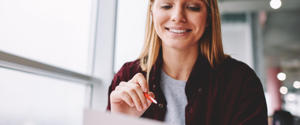 A smiling woman sitting at a table, filling out a rental application form. The scene captures her positive attitude and focus, reflecting an important step in the process of securing a new home or apartment.