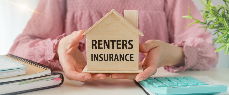 Hands holding a wooden house model with 'Renters Insurance' written on it, symbolizing renter's insurance as a hidden cost of renting.