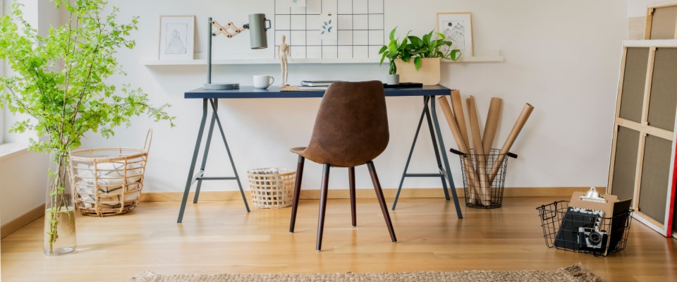 A brown chair at a desk in a workspace featuring white walls, a cozy carpet, and minimalist decor. 