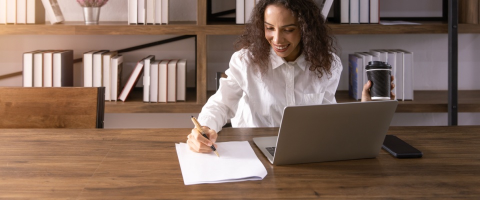 A woman author sitting in a creative workspace, happily writing down new ideas on paper. The scene captures her focus and joy in the process of crafting her thoughts, surrounded by a comfortable and inspiring environment.