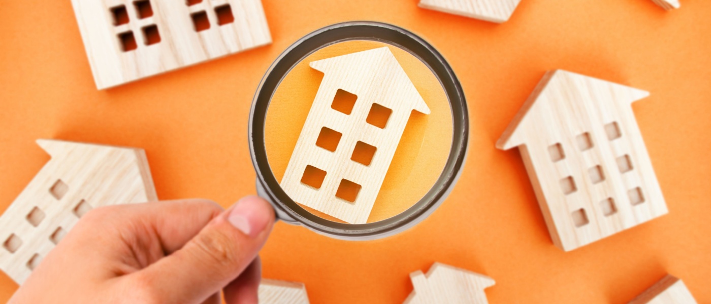 Magnifying glass and miniature wooden buildings to symbolize searching for an apartment for rent.