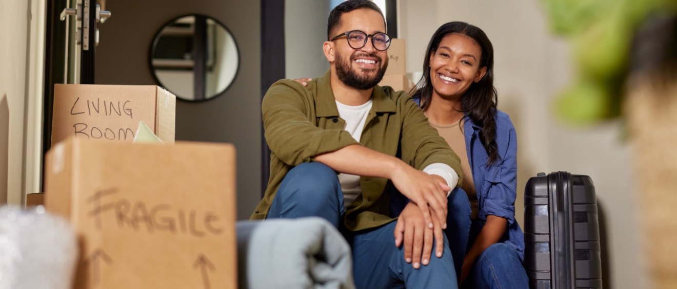 A smiling man and a woman sitting together on the stairs of their new home after a day of moving. The scene highlights the importance of planning, including setting a budget for moving.