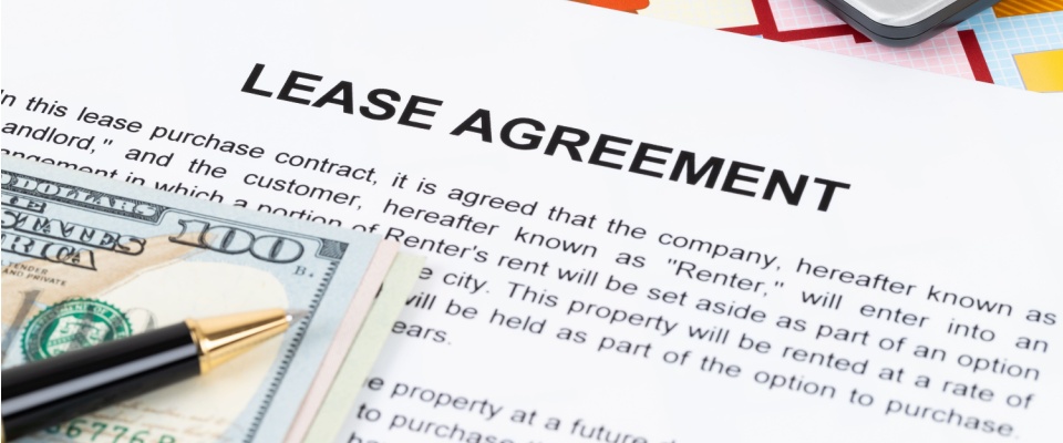 A close-up of the first page of a lease agreement, with parts of the first paragraph visible, as well as a ballpoint pen set on top of a stack of bills.