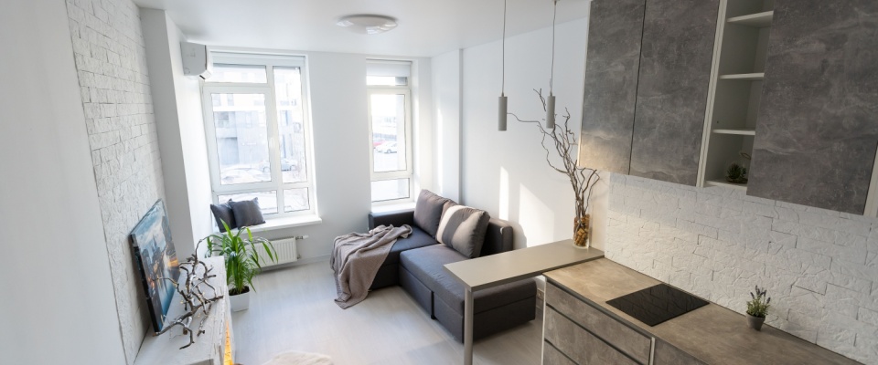 The kitchen and living area in a studio apartment, with the large windows letting in plenty of natural light into the space.
