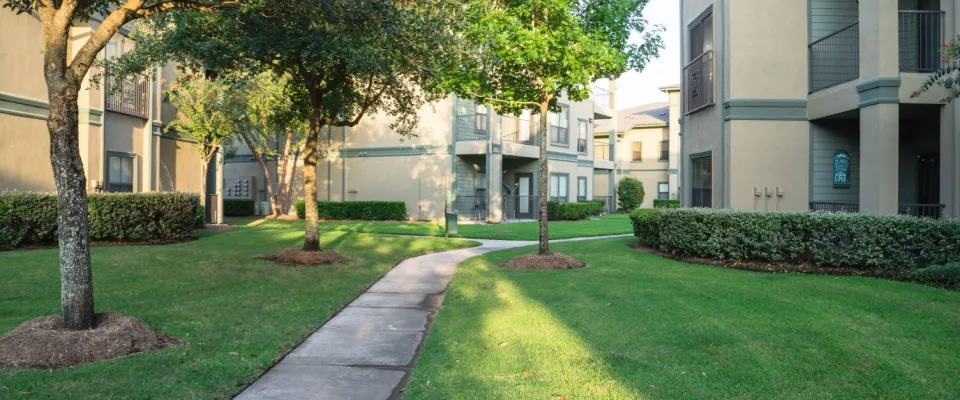 Clean lawn and tidy oak trees along the walk path through a garden-style apartment building in a suburban area in Texas, US.