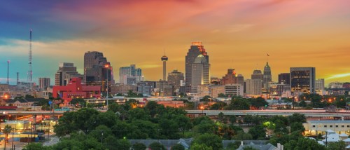 The skyline in downtown San Antonio, TX, pictured at sundown, with the city’s buildings set against a colored sky.