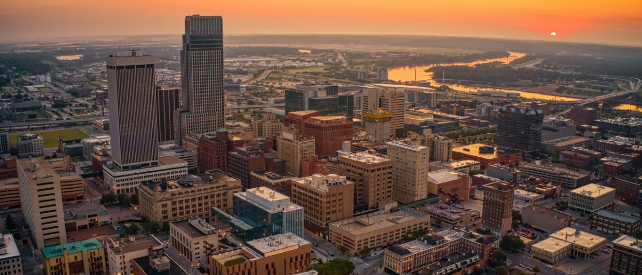 An aerial view of the downtown area in Omaha, pictured at sunset, with its buildings set against an orange sky.