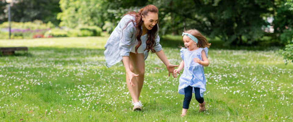 Happy mother and her young daughter playing together in a lush green park or garden on a sunny summer day.