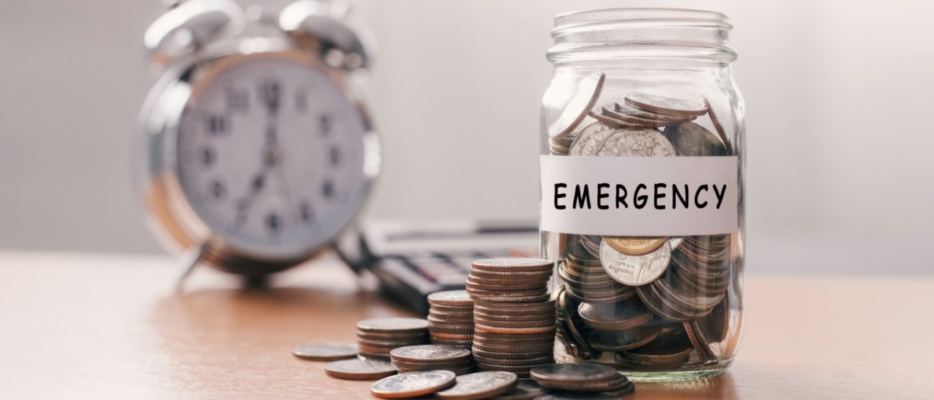 Glass jar filled with coins next to a piggy bank, symbolizing saving money for emergencies.