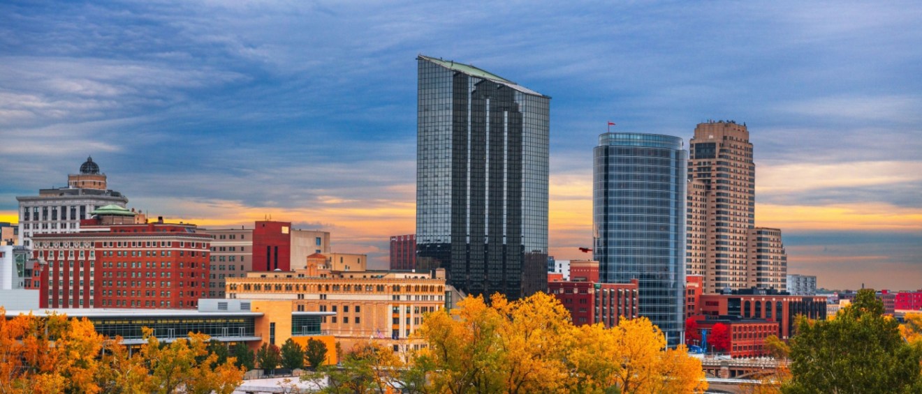 Downtown Grand Rapids, MI, skyline featuring modern high-rises with apartments, historic buildings, beautiful autumn foliage, and a colorful sunset.