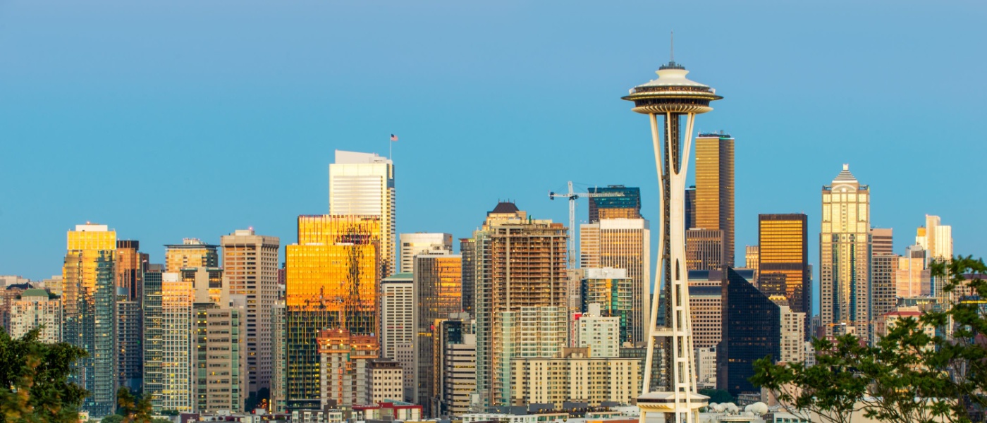 Find affordable neighborhoods in Seattle, WA. Seattle skyline featuring the Space Needle and high-rise buildings illuminated by golden sunlight against a clear blue sky.