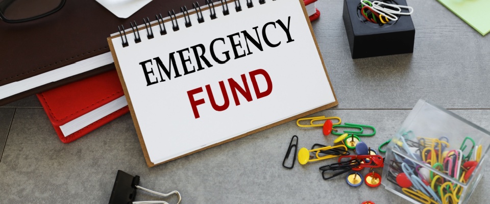 Two notepads on a work table with 'EMERGENCY FUND' written on one of the pages.