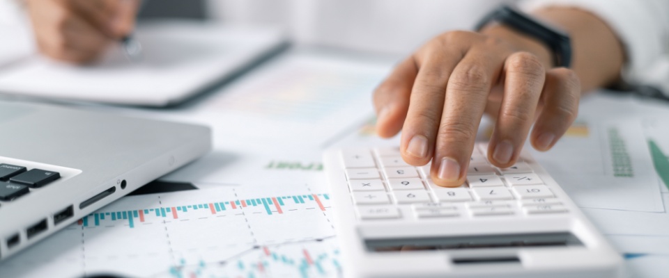 Businesswoman calculating finances at a desk in a home office, using a calculator and reviewing accounting documents.
