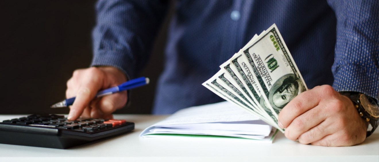 Close up of a man's hands holding money and calculating a rental application fee on a calculator.