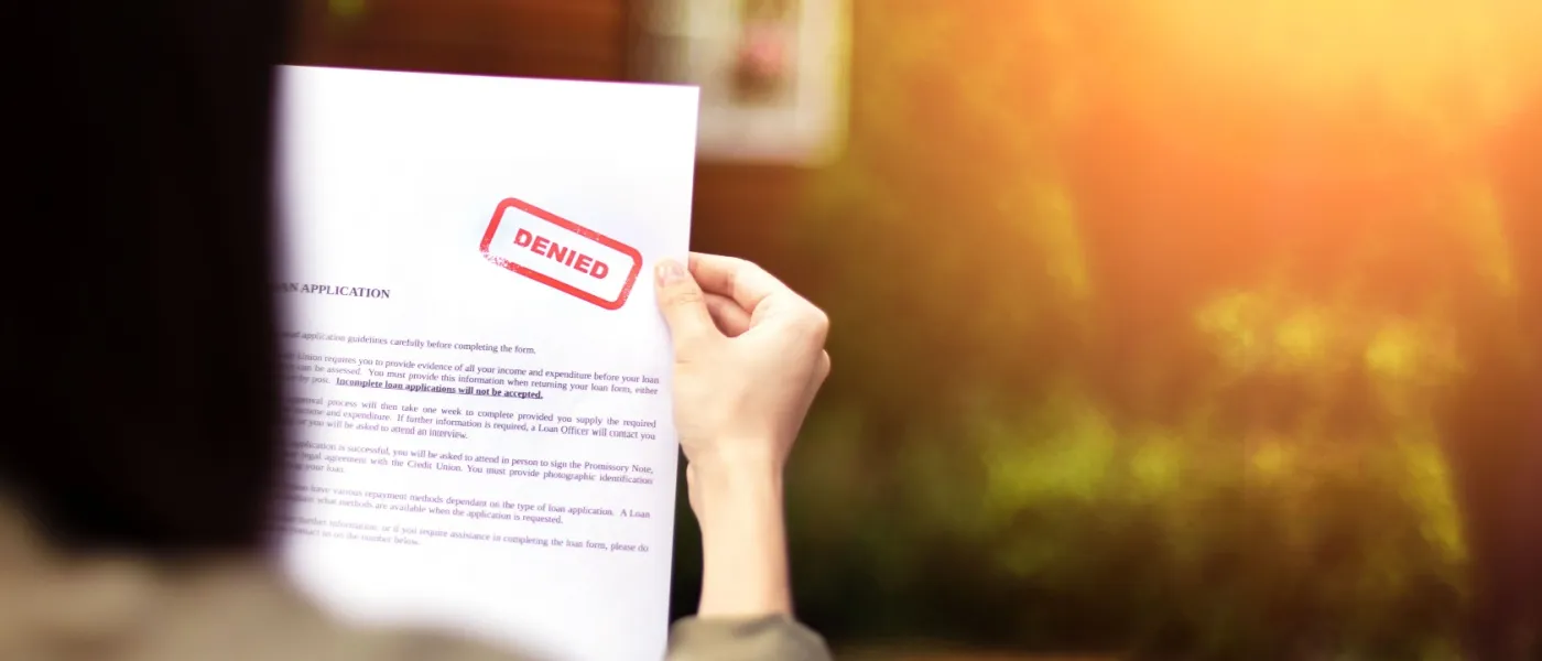 Hands holding a rental application letter with a bold red 'denied' stamp, indicating rejection after a rental application form submission.