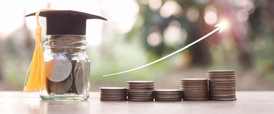 A glass bottle with a graduation hat and a stack of coins with rising arrow icons symbolize saving money for education, student loans, scholarships, and tuition fees.
