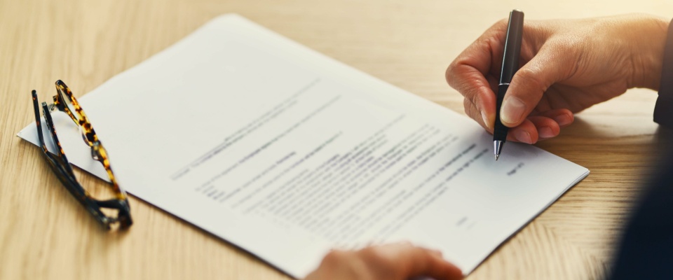 An unrecognizable businesswoman carefully reviewing the fine print while completing paperwork at a desk, emphasizing the importance of understanding details in student loans.