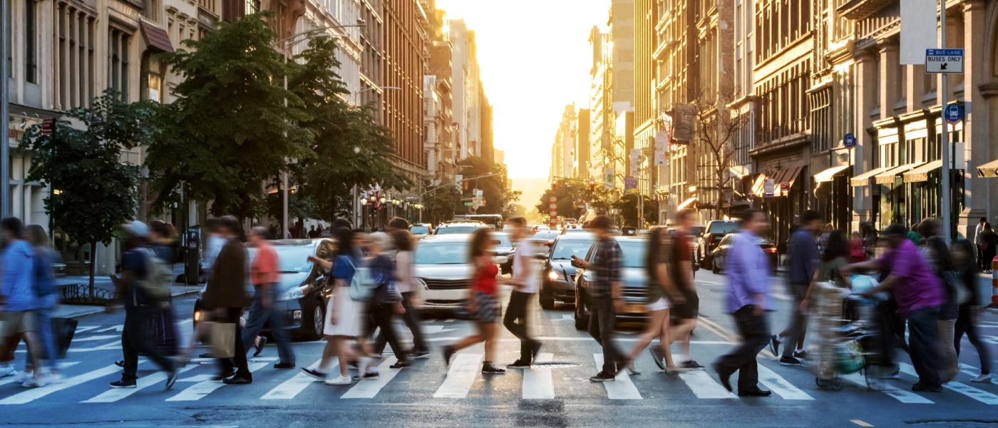 A busy city street with blurred pedestrians crossing at a crosswalk during sunset, symbolizing the fast-paced nature of securing an apartment in a competitive rental market.
